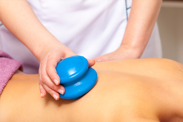 Massage therapist carefully removing cupping therapy cups from a client’s back