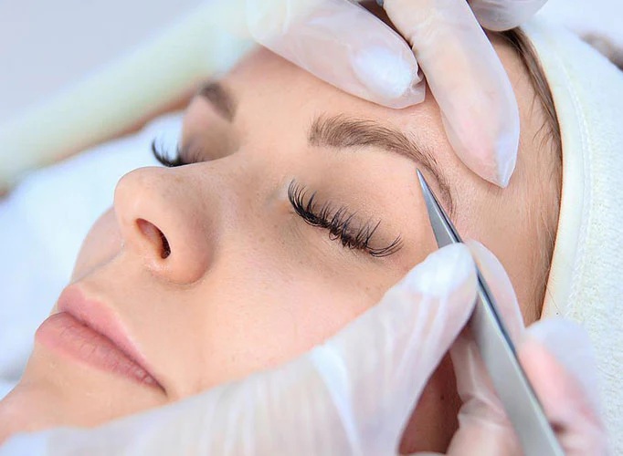 Professional brow shaping using tweezers at Rowan & Peridot Collective